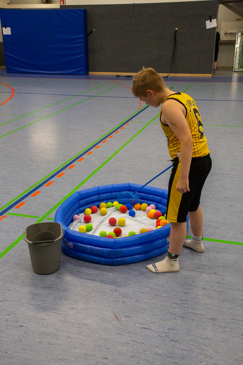 Junge fischt Bälle aus Pool in Turnhalle