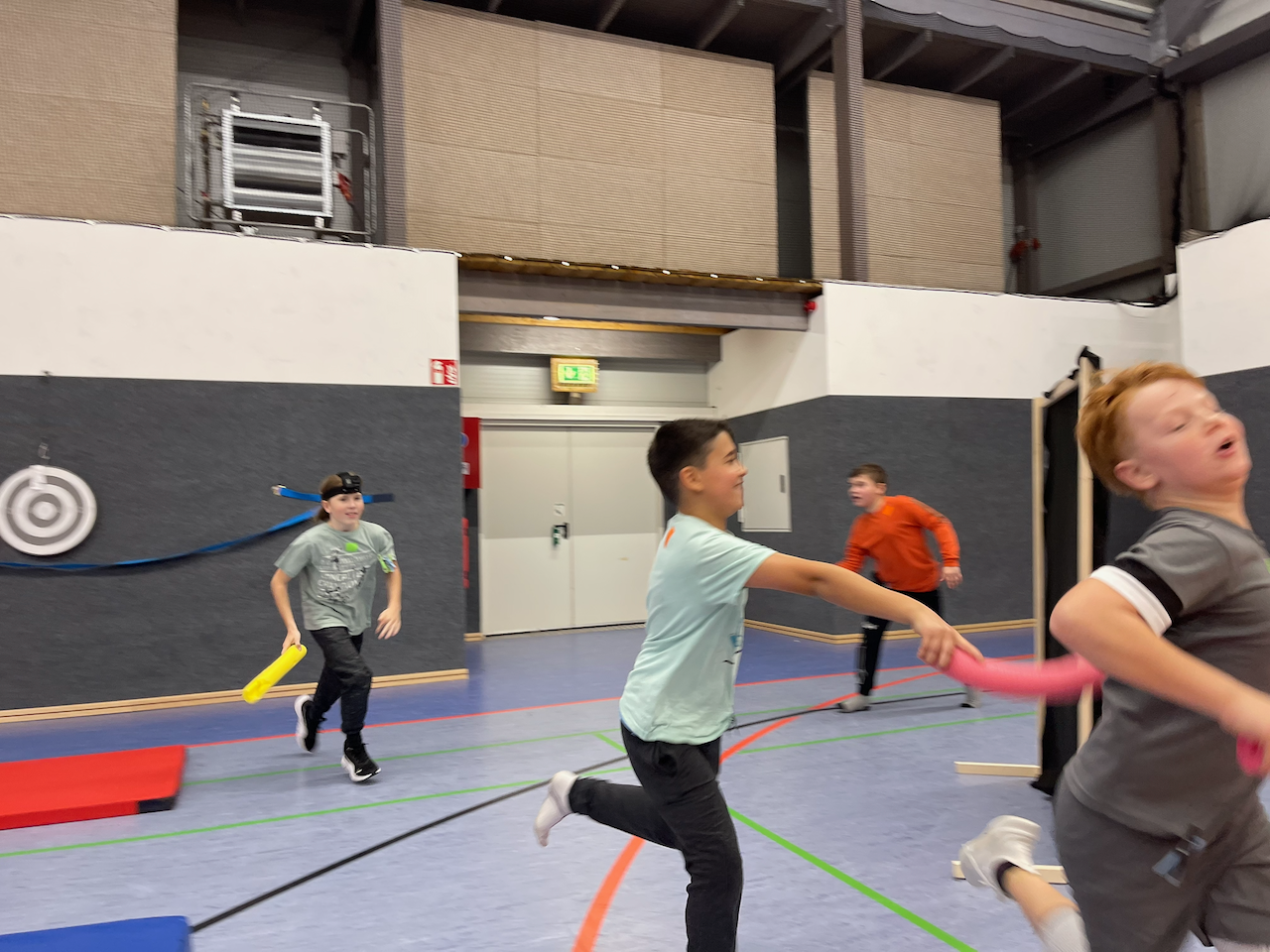 Kinder spielen mit Poolnudelstücken in einer Turnhalle