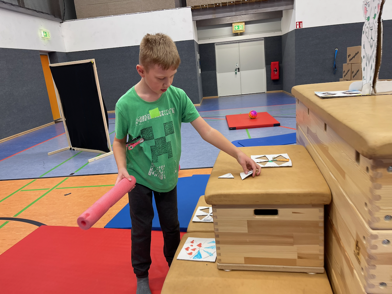 Junge legt ein Puzzleteil auf eine Treppe aus Kästen in einer Turnhalle