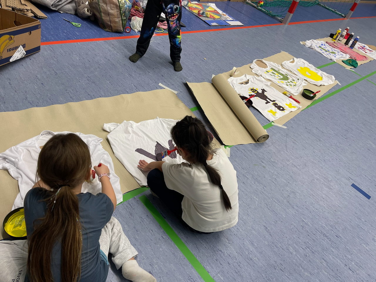 Drei Mädchen bemalten T-Shirts in einer Sporthalle