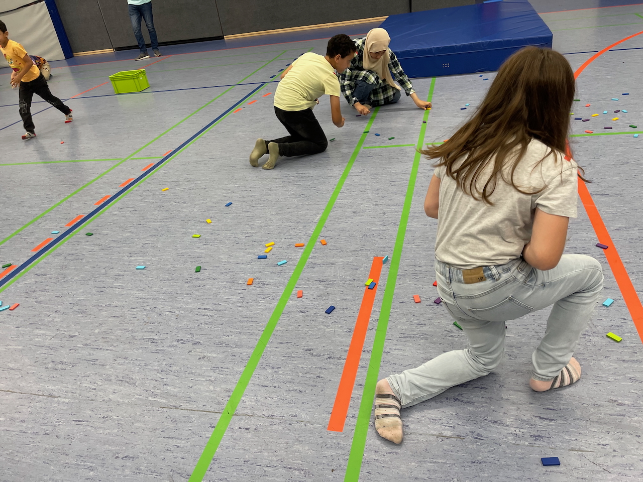 Kinder sammeln Dominostein in einer Sporthalle