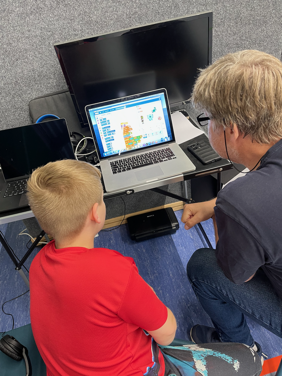 Ein Junge und ein Mann vor einem Bildschirm mit einem Script in Scratch