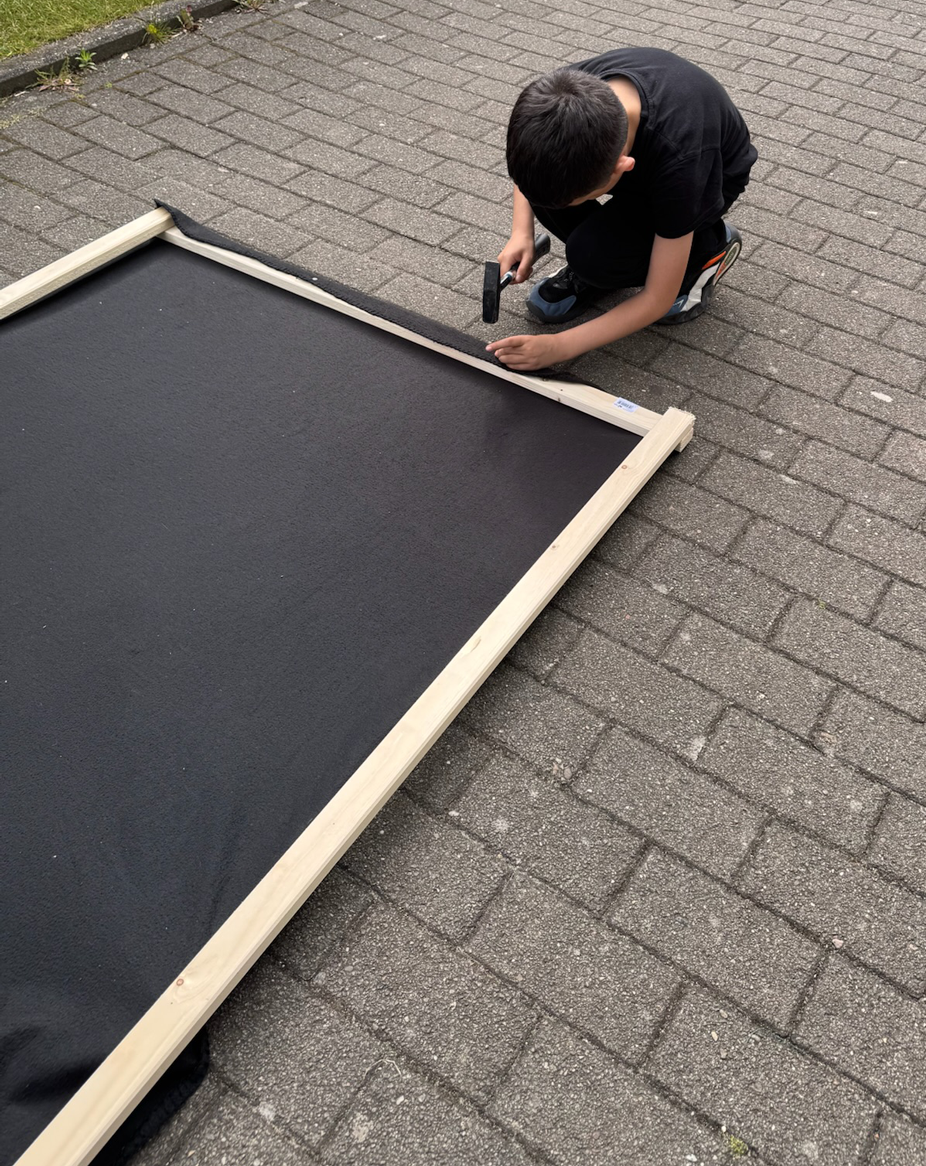 Ein Junge nagelt eine schwarze Decke auf einen Rahmen.