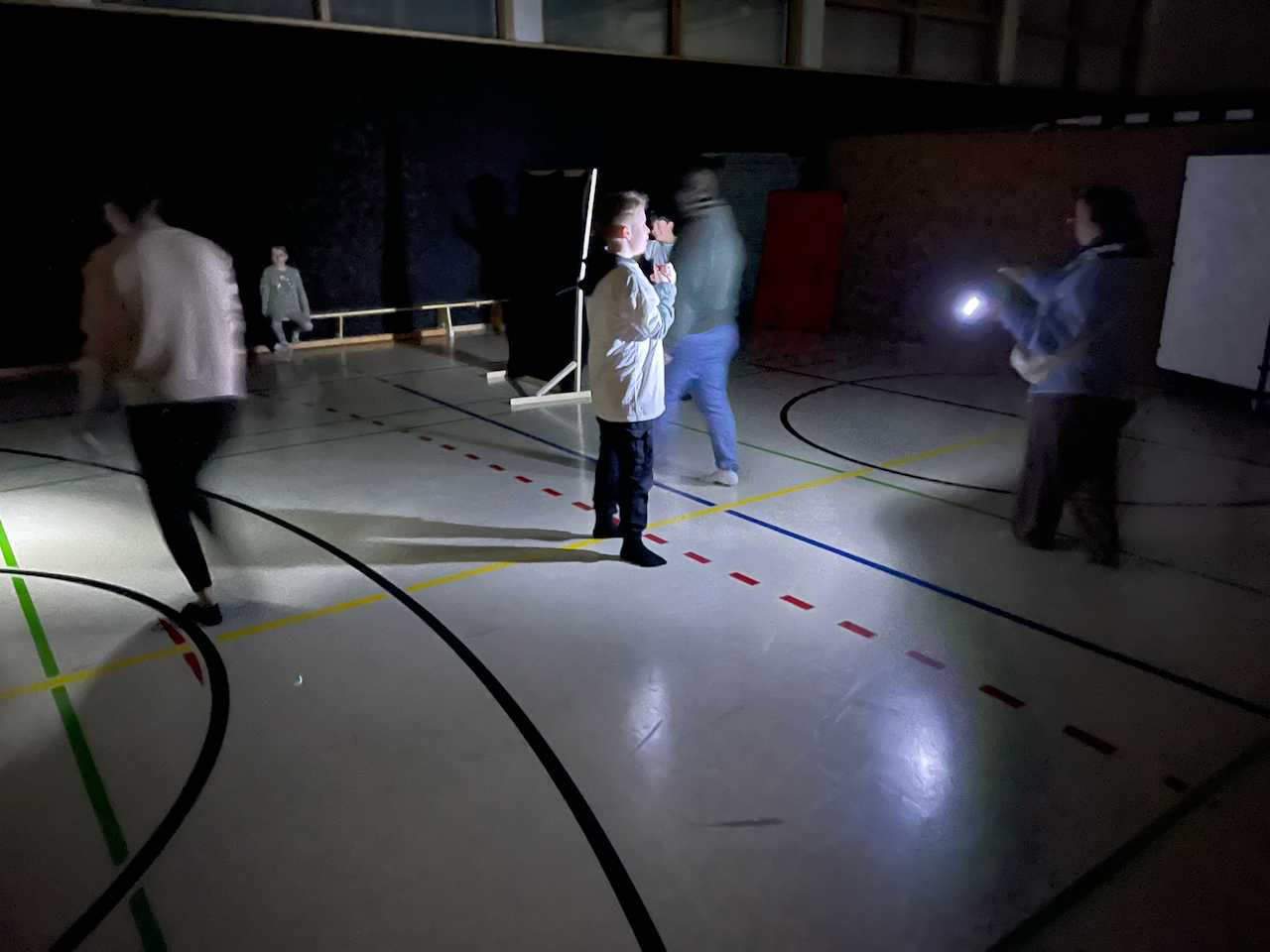 In einer dunklen Turnhalle wird ein Junge mit einer Taschenlampe angestrahlt
