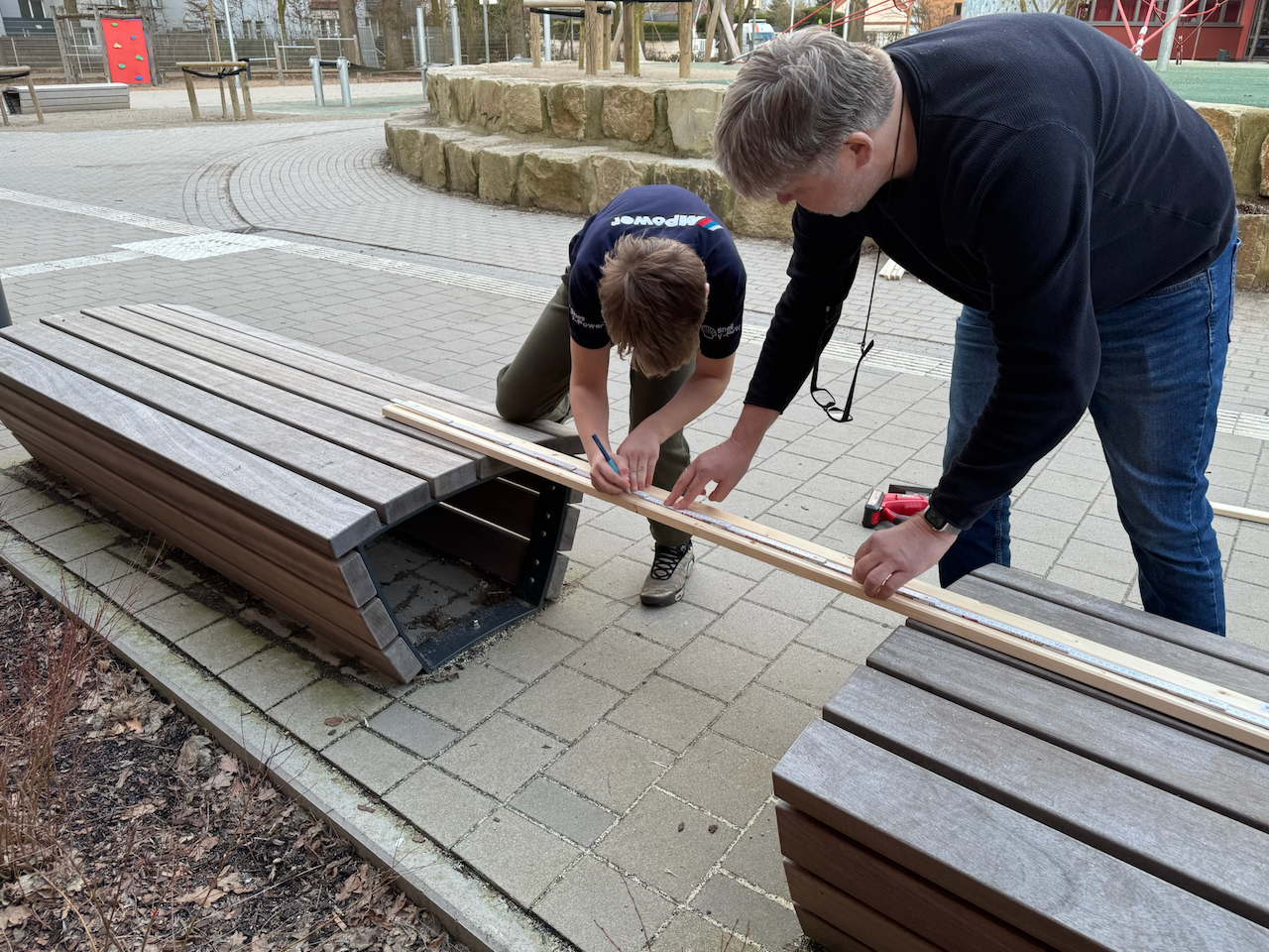 Mann und Junge: Zwischen zwei Schulhofbänken Anzeichnen von Brett zum Bau von Stellwänden.