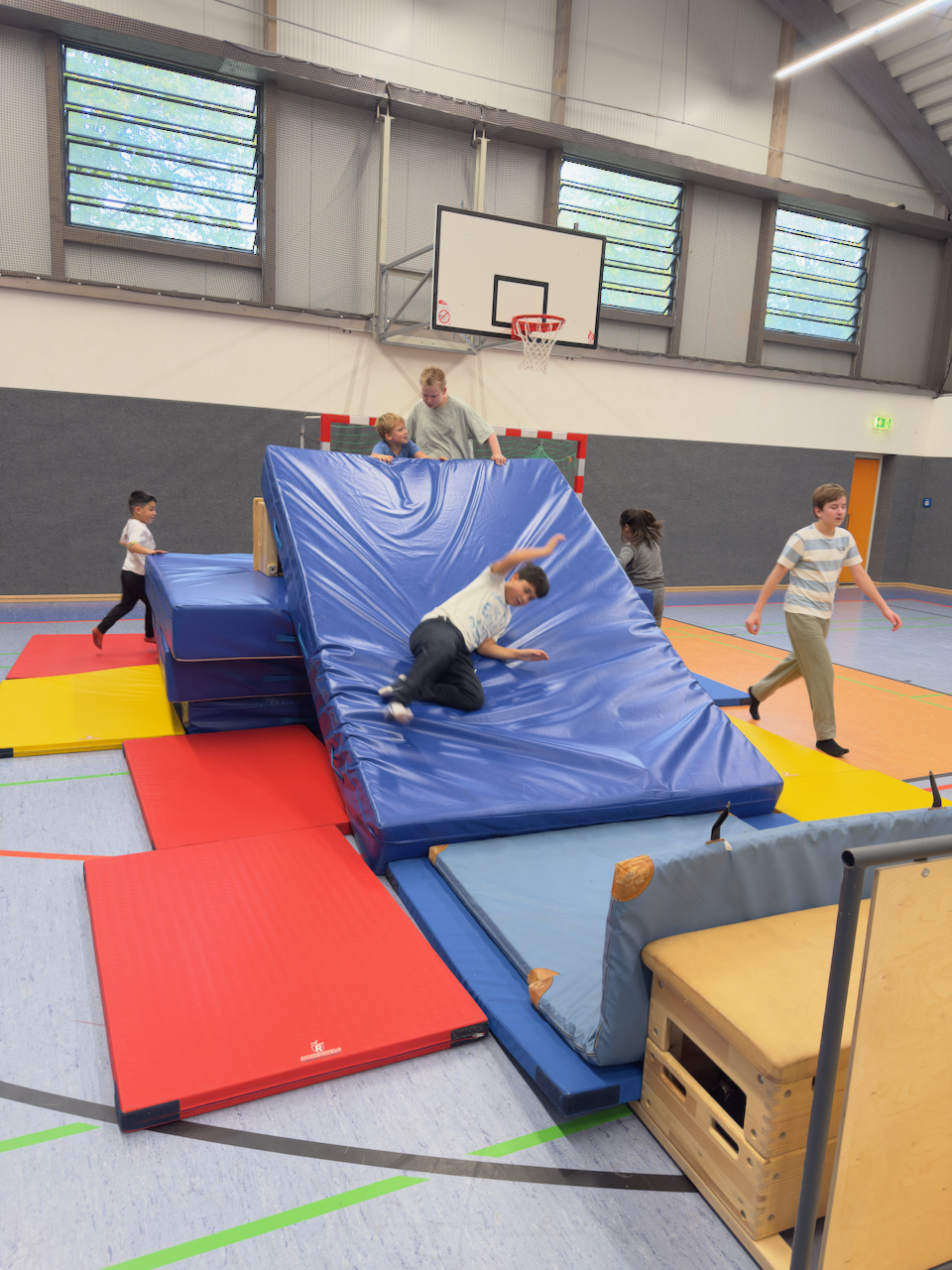 Kinder auf einer selbstgebauten Mattenrutsche in einer Turnhalle