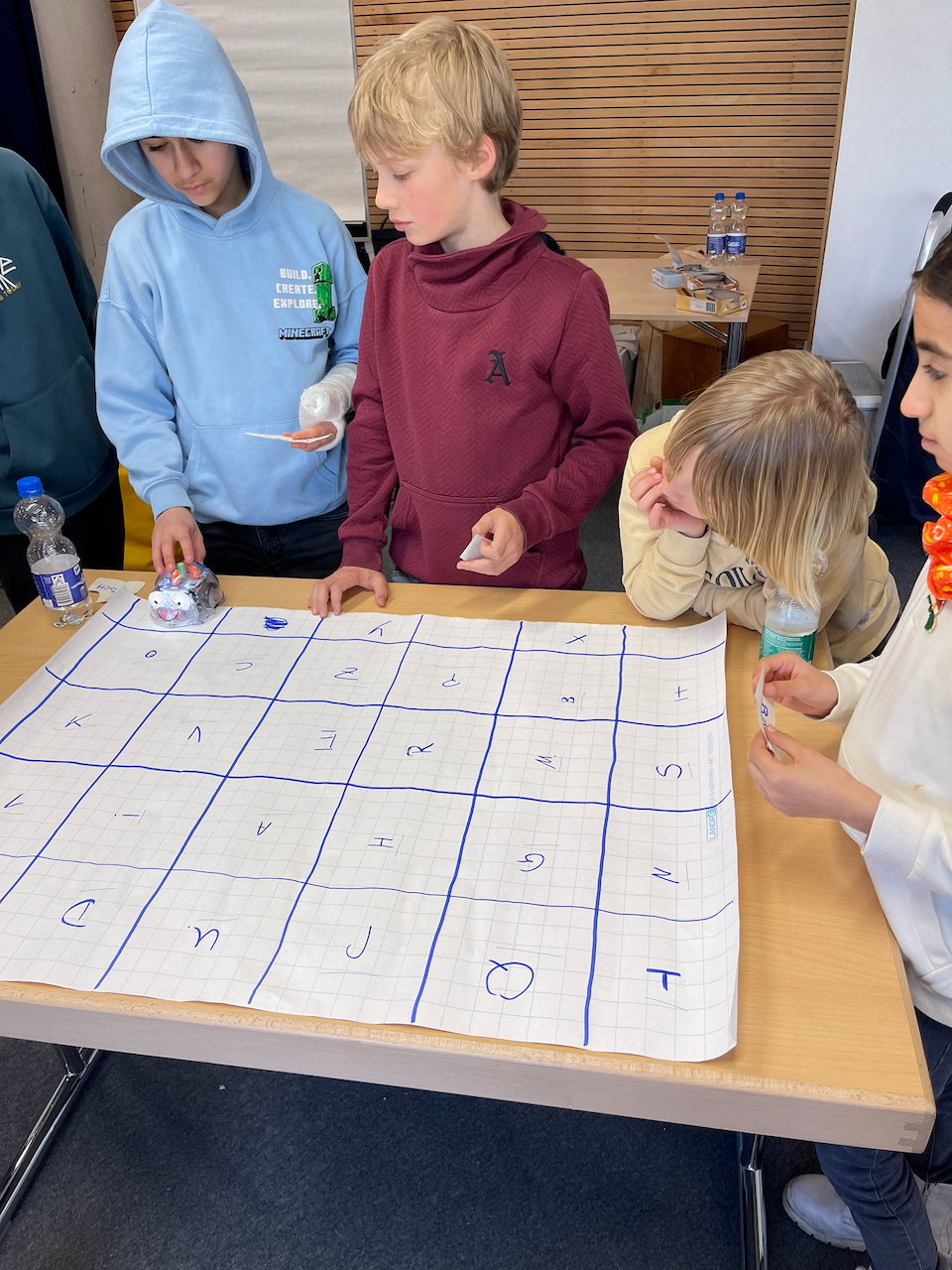 Kinder um ein Feld mit Buchstaben, worauf ein Bluebot fährt.